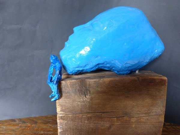 Blauer Kopf aus Beton mit sitzender modellierter Figur   auf Bauholz